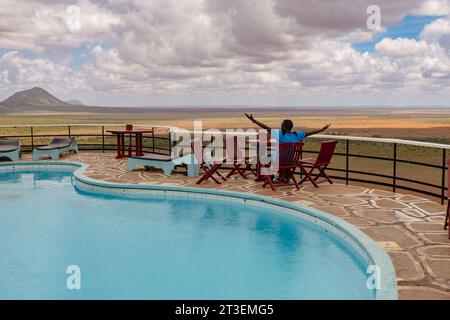 Ein Mann neben einem Swimmingpool vor einem malerischen Aussichtspunkt in einer Lodge im Tsavo East Nationa Park, Kenia Stockfoto