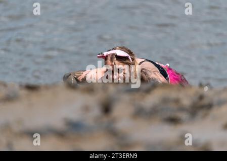 Junge Frau krabbelt am schlammigen, rutschigen Flussufer des River Blackwater nahe dem Ziel des Maldon Mud Race 2019 hinauf. Mit Schlamm bedeckt Stockfoto