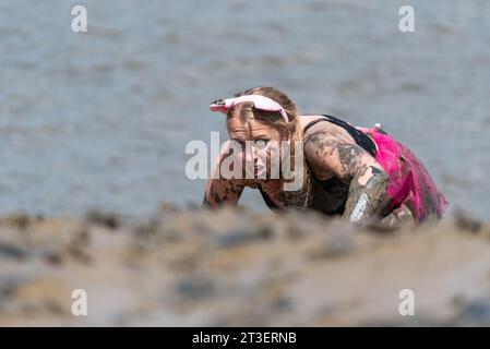 Junge Frau krabbelt am schlammigen, rutschigen Flussufer des River Blackwater nahe dem Ziel des Maldon Mud Race 2019 hinauf. Mit Schlamm bedeckt Stockfoto