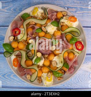 REZEPT FÜR MELONE, MOZARELLA, BASILIKUM UND GERÄUCHERTEN SCHINKENSALAT, GURKENSCHEIBE, ORANGENVINAIGRETTE Stockfoto