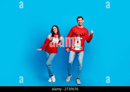 Foto in voller Länge von schönen jungen Ehegatten, die tanzen, haben Spaß gekleidete Weihnachtsdekoration rote Pullover isoliert auf blauem Hintergrund Stockfoto