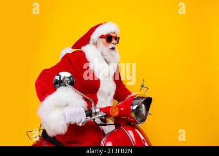 Porträt des lustigen weihnachtsmanns Fahrt Moped schnelle Reise um die Welt Lieferung weihnachtskurier isoliert auf gelbem Hintergrund Stockfoto