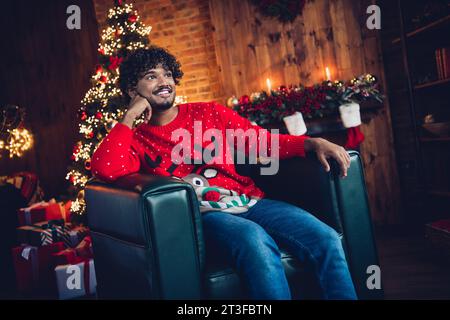 Foto des jungen süßen träumenden Mannes sitzender Lederstuhl santa claus Helfer Touch Wange wartet auf weihnachtswunder Geschenke im Wohnzimmer Stockfoto