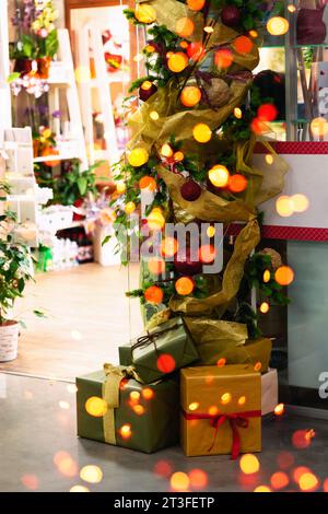 Geschmückter Ladeneingang zu Weihnachten. Girlande, Lichter und Boxen mit Bögen. Silvester-Schaufenster mit einer Fichtengirlande mit Spielzeug und Lichtern und b Stockfoto