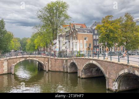 Niederlande. Bewölkter Sommertag. Alte Steinbrücken auf den Kanälen von Amsterdam. Typisch holländische Häuser mit tanzenden Fassaden auf dem Damm. Teenager o Stockfoto