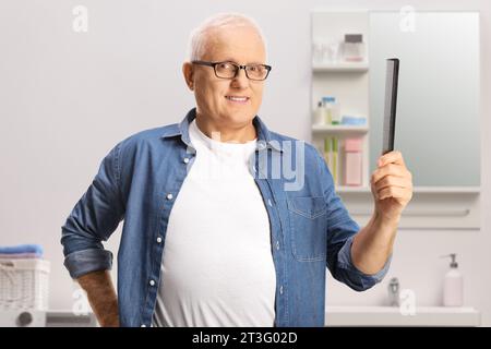 Reifer Mann mit weißem Haar, der im Badezimmer einen Haarkamm hält Stockfoto
