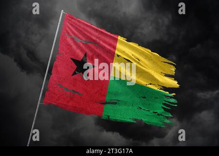 Guinea-Bissau zerrissene Flagge auf dunklem Himmel Hintergrund. Stockfoto