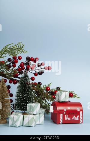 Komposition mit vielen Geschenken, einem Zweig der stechpalme mit seinen roten Beeren, einem Briefkasten des weihnachtsmanns und einem weihnachtsbaum vor einem leuchtenden himmelblauen Hintergrund. Stockfoto