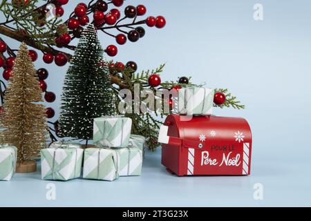 Komposition mit vielen Geschenken, einem Zweig der stechpalme mit seinen roten Beeren, einem Briefkasten des weihnachtsmanns und einem weihnachtsbaum vor einem leuchtenden himmelblauen Hintergrund. Stockfoto