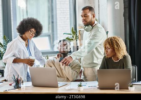 Ein durchdachtes Team von Freunden in kühnen Gewändern, die sich ein Notebook ansehen und über Projekt und Arbeitsprozess sprechen Stockfoto