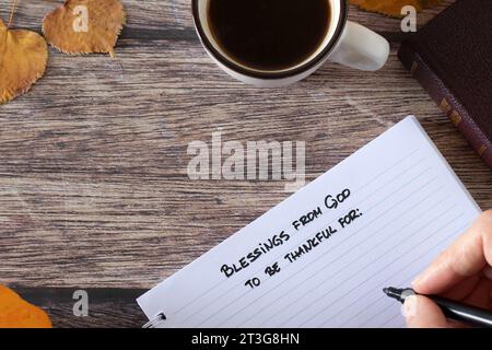 Handschriftlich inspirierender Text „Segen von Gott zum dankbar sein“ in Notizbuch, heilige Bibel, Kaffeetasse und Herbstblätter auf Holztisch. Draufsicht. Stockfoto