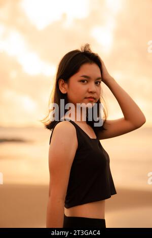 Ein asiatischer Teenager mit einem süßen Gesicht in schwarzer Kleidung lächelt und genießt die wunderschöne Landschaft am Strand vor Sonnenuntergang Stockfoto