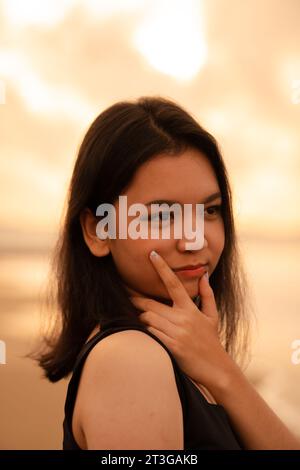 Eine asiatische Teenagerin mit schwarzem Hemd und schwarzem Haar hat ein süßes Gesicht, wenn sie lächelt und die Aussicht vor Sonnenaufgang genießt Stockfoto