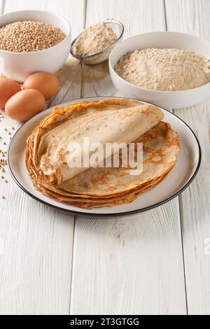 Traditionelle französische Buchweizen-Galettes Bretonpfannkuchen auf einem Tisch mit Mehl, Müsli und Eiern aus der Nähe auf dem weißen Holztisch. Vertikal Stockfoto