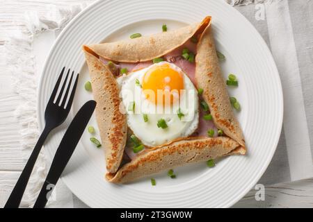 Bretonische Galette, Galette Sarrasin, Buchweizenkrepe, mit Spiegelei, Käse, Schinken Nahaufnahme auf dem Teller auf dem Tisch. Horizontale Draufsicht von oben Stockfoto