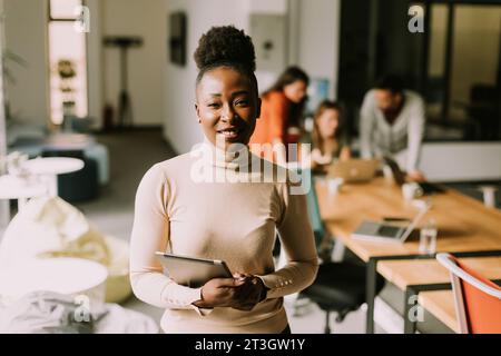 Junge afroamerikanische Frau, die mit einem digitalen Tablet vor ihrem Team im modernen Büro steht Stockfoto