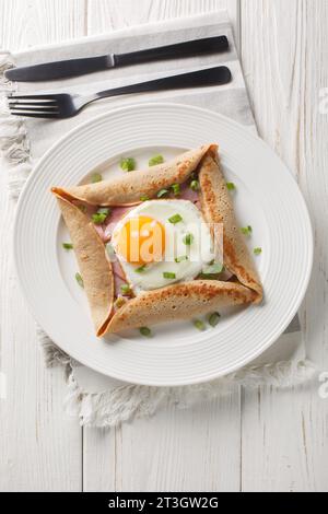 Hausgemachtes Buchweizen-Kreppegalette mit Ei, Schinken und grüner Zwiebelnaht auf dem Teller auf dem Tisch. Vertikale Draufsicht von oben Stockfoto