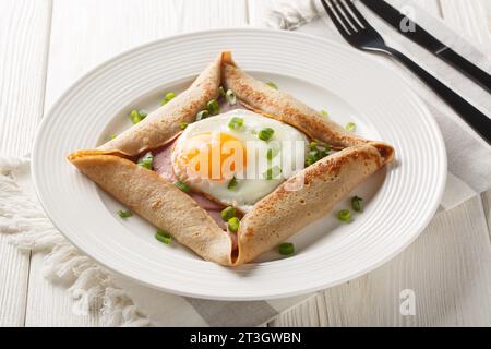 Bretonische Krepé, herzhafte Buchweizen-Galettes Bretons mit Spiegelei, Käse, Schinkennaht auf dem Teller auf dem Tisch. Horizontal Stockfoto