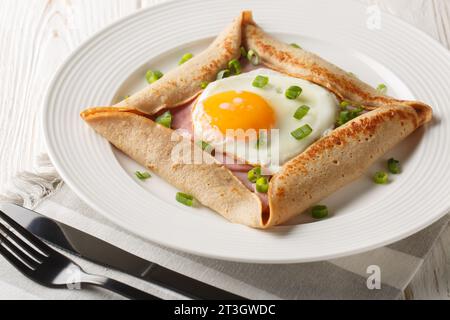 Bretonische Galette, Galette Sarrasin, Buchweizenkrepe, mit Spiegelei, Käse, Schinken Nahaufnahme auf dem Teller auf dem Tisch. Horizontal Stockfoto