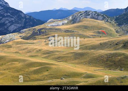 Montenegro, Durmitor-Nationalpark, der von der UNESCO zum Weltkulturerbe erklärt wurde, Straße zwischen Zabljak und Pluzine, bergige Landschaft mit Hirtenhäusern und einem roten Gleitschirmflieger Stockfoto