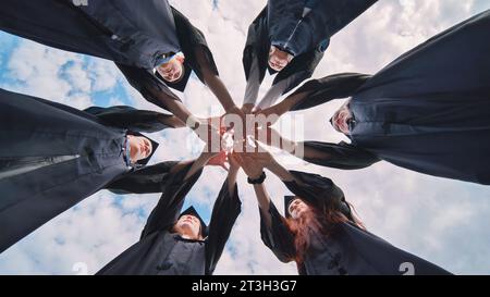Team von College- oder Universitätsstudenten, die den Abschluss feiern. Gruppe glücklicher erfolgreicher Absolventen in akademischen Hüten und Gewändern, die im Kreis stehen und Stockfoto
