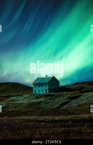 Fantastische Landschaft von Aurora Borealis oder Nordlichter, die über verlassenen skandinavischen Haus auf einem Hügel in abgelegener Lage in der Nacht in Island leuchten Stockfoto