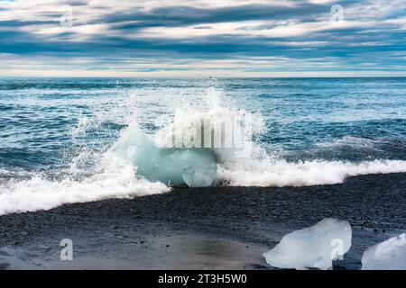 Die Welle stürzt mit Eisberg am schwarzen Sandstrand am Diamond Beach im Sommer im Süden Islands Stockfoto
