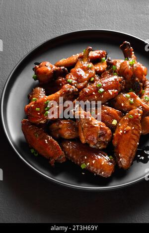Süße und würzige Hähnchenflügel auf dem Teller mit dunklem Steinhintergrund. Nahaufnahme Stockfoto