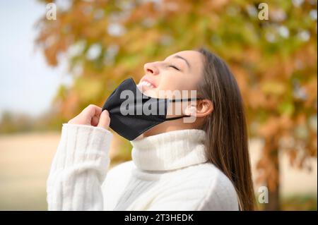 Profil einer entspannten Frau, die Maske auszieht und frisch atmet Luft in einem Park in Coronavirus Zeiten Stockfoto