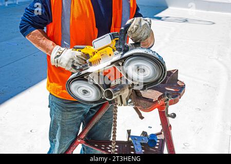 Ein Bauarbeiter schneidet mit einer tragbaren Bandsäge Edelstahlrohre auf dem Dach einer industriellen Kühlanlage (Kühllager). Stockfoto