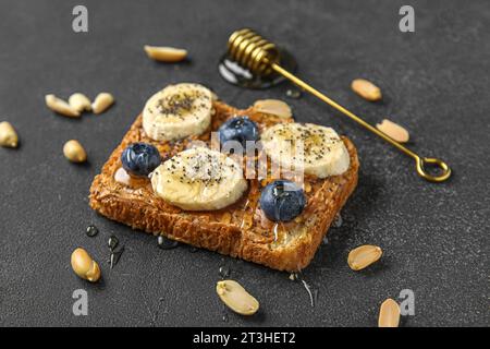 Toast mit Erdnussbutter, frischem Obst und Honig auf schwarzem Hintergrund Stockfoto