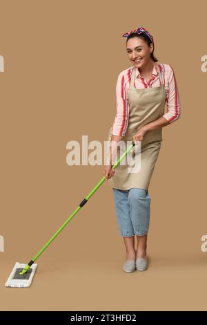 Porträt einer glücklichen jungen Hausfrau in Schürze mit Wischtuch auf braunem Hintergrund Stockfoto