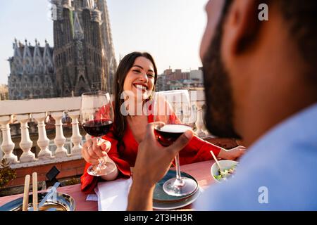 Multirassisch wunderschönes glückliches Paar von Liebhabern, die auf dem Dachbalkon in der Sagrada Familia, Barcelona, ausgehen - multiethnische Leute, die einen romantischen Aperitif genießen Stockfoto