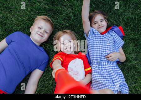 Kinder liegen und lachen auf dem grünen Rasen. Niedliche Kinder haben draußen auf der Wiese Spaß. Kleine Freunde in lässiger Kleidung haben eine tolle Zeit miteinander. Stockfoto