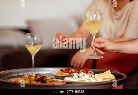 Zwei Gläser kühlen Sekt und Teller mit verschiedenen Snacks auf einem runden Metall-Couchtisch. Weiße Teller mit Schinkenscheiben, Salami, Kapern, Oliven und Stockfoto