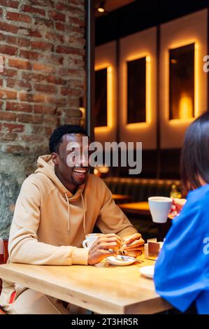 Lächelnder Afroamerikaner, der Spaß mit weiblichen Freunden hat, die in einem Café Kaffee trinken Stockfoto