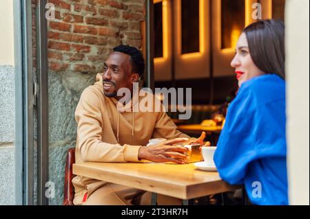 Zwei multiethnische Freunde, die gemeinsam einen Kaffee genießen, sitzen an einem Tisch Stockfoto