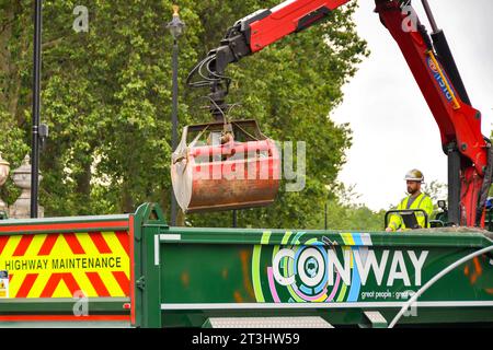 London, England, Großbritannien - 28. Juni 2023: Bauarbeiter, die einen Hydraulikkran auf der Rückseite eines Kipperlasters betreiben, um Schutt aus der Straßenverbesserung zu heben Stockfoto