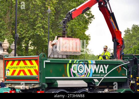 London, England, Großbritannien - 28. Juni 2023: Bauarbeiter, die einen Hydraulikkran auf der Rückseite eines Kipperlasters betreiben, um Schutt aus der Straßenverbesserung zu heben Stockfoto