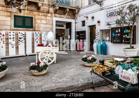 Eine Auswahl an Obst und Gemüse, die vor einem Geschäft verkauft werden, in dem eine Sammlung farbenfroher Töpferwaren in Ostuni, Otaly, verkauft wird. Stockfoto