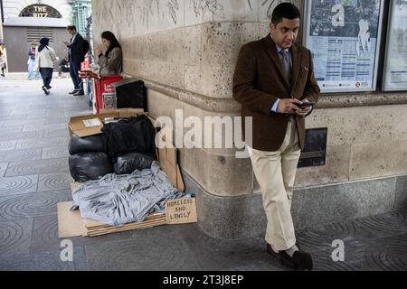 Ein Geschäftsmann überprüft sein Smartphone vor der U-Bahnstation Green Park, während hinter ihm Obdachlose in der Winternacht wohnen. Stockfoto