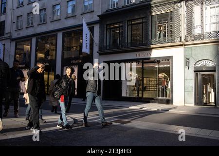 Touristen, die teilweise von der Herbstsonne geblendet werden, während sie an PRADA auf der Old Bond Street in London, England, Großbritannien vorbeilaufen Stockfoto