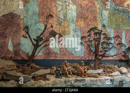 Guatemala, La Antigua - 20. Juli 2023: Jade Maya Museum. Landschaft mit 3 kleinen Statuen, von denen 2 Menschen in Strandlandschaft vor Wandmalerei stehen Stockfoto