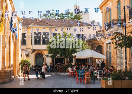 Griechische Flaggen fliegen über den Restaurantgästen, die an einem sonnigen Nachmittag im Freien in der Altstadt von Nikosia, Zypern, speisen Stockfoto