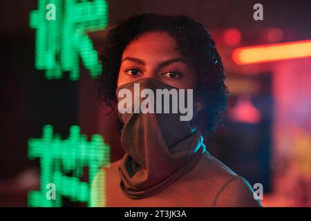 Hübsches afroamerikanisches Mädchen mit einem Gesicht, das halb mit Maske bedeckt ist und in die Kamera im Café oder in der Bar blickt, mit grünen Hieroglyphen, was beste Ramen bedeutet Stockfoto