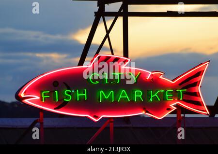 Ein großer Neonfisch, der für den City Fish Market wirbt, wird vor dem Abendhimmel über dem Pike Place Market in Seattle beleuchtet Stockfoto