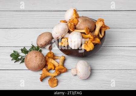 Schüssel mit verschiedenen Pilzen und Petersilie auf weißem Holztisch Stockfoto