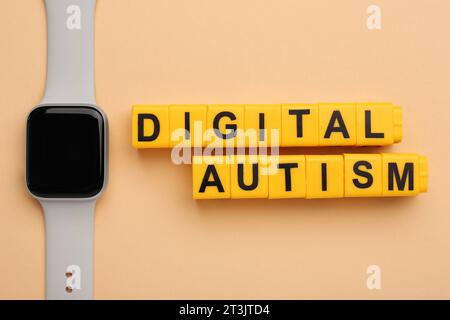 Phrase Digital Autismus aus gelben Würfeln und Smartwatch auf beigefarbenem Hintergrund, flache Lay. Suchtverhalten Stockfoto