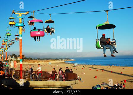 Die Menschen genießen einen sonnigen Sommerurlaub bei einer Fahrt mit dem Skilift über den Santa Cruz Boardwalk und den Strand Stockfoto