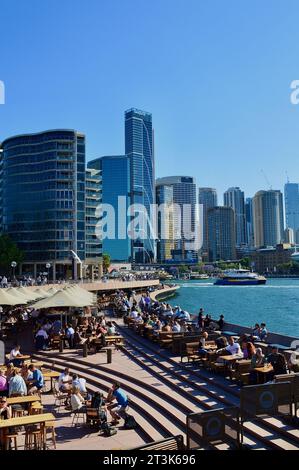 Eine vertikale Gruppe von Menschen in einem Café vor dem Stadtbild von Sydney, Australien an einem sonnigen Tag Stockfoto